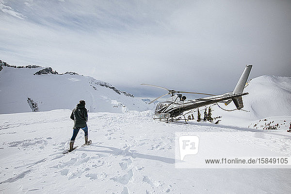 Abenteuerlustige Frau mit Schneeschuhen in Richtung Hubschrauber.
