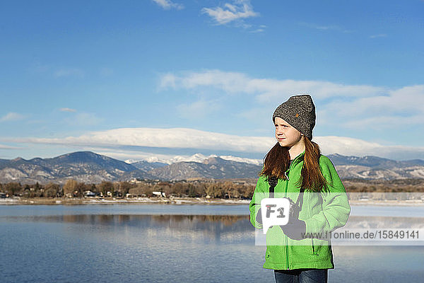 Junges rothaariges Mädchen mit Kamera an einem See in den Bergen