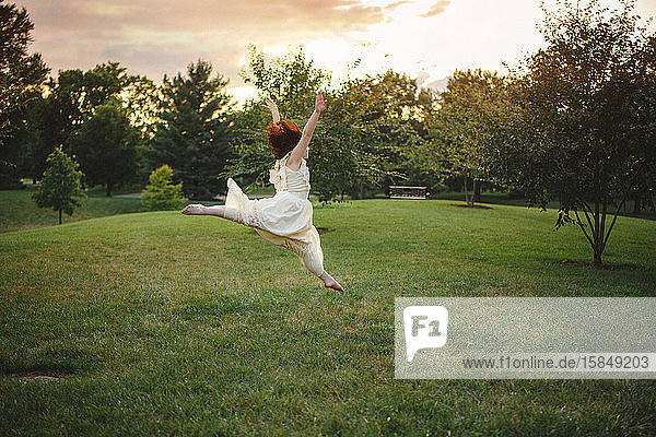 Eine fröhliche junge Tänzerin springt bei Sonnenuntergang in einem Park