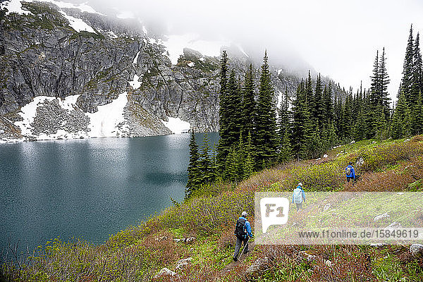 A group of people hike around a beautiful alpine lake on a cloudy  rainy summer day in the Coast Mountains around Pemberton  British Columbia.
