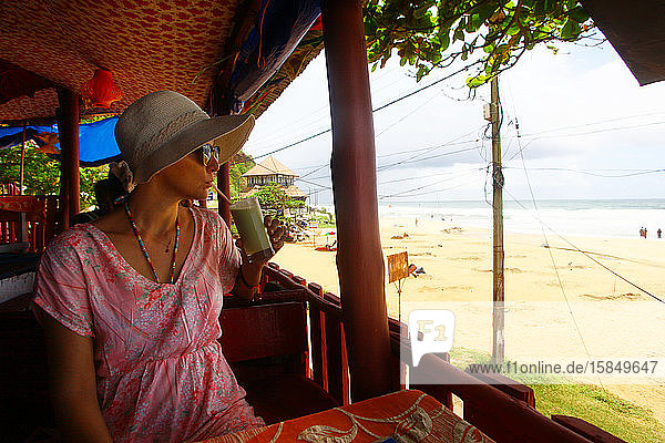 Frau  die Smoothie in einem Café am Strand von Varkala in Indien trinkt.