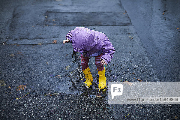 Ein kleines Mädchen  das an einem regnerischen Tag in Pfützen plantschend Spaß hat.