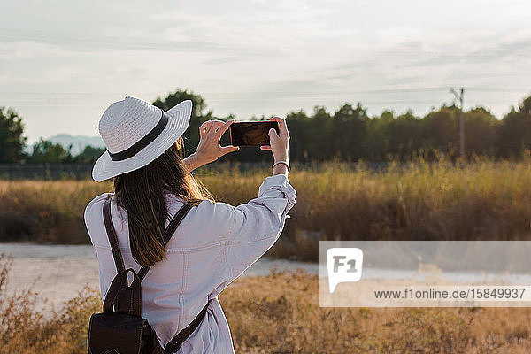 Junge Frau macht ein Foto mit ihrem Smartphone auf einem Feld. Abenteuer  Technik