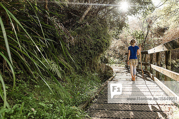 Zwischenmenschliches Mädchen geht auf hölzernem Waldweg in Neuseeland