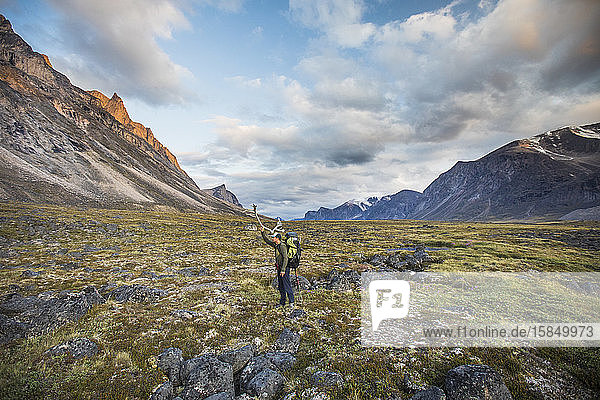 Backpacker standing in mountain pass holding Caribou antler on head.