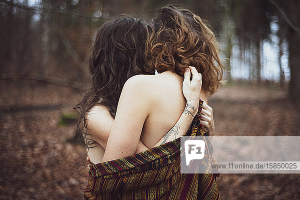 gesichtsloses Porträt eines jungen lesbischen Paares  das sich im goldenen Wald umarmt