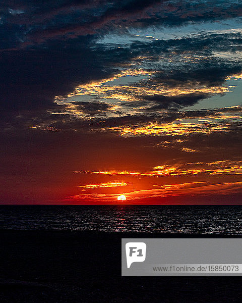 Launischer Himmel über dem Strand  während die Sonne unterhalb des Horizonts untergeht.