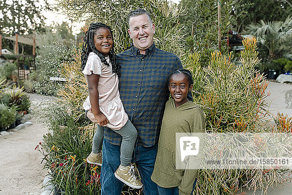 Joyful white dad holding one daughter and hugging other daughter