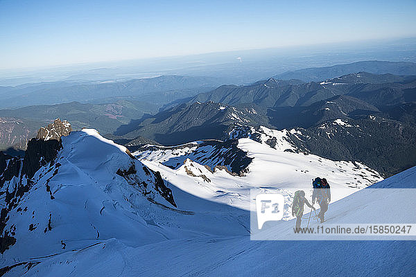 Two athletes hike up a glacier on Mt. Baker in the shadow of the summit.