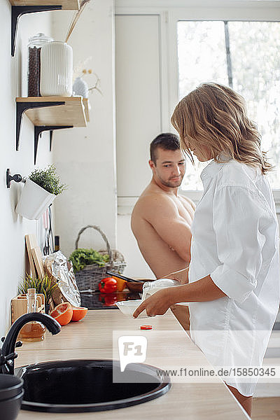 Junges romantisches Paar auf heller moderner Küche. Mädchen bereitet Müsli zu