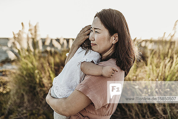 Mid view of happy mom embracing young toddler at beach during sunset