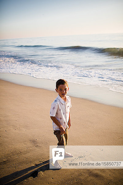 Junge Junge steht bei Sonnenuntergang am Strand