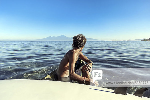 Seitenansicht eines anonymen Mannes mit Surfbrett im Ruderboot sitzend