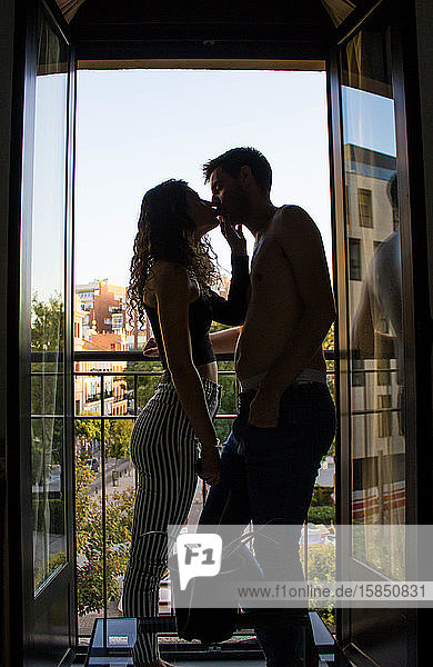 Zu Hause küssendes Paar  das bei geöffnetem Fenster im Rahmen steht