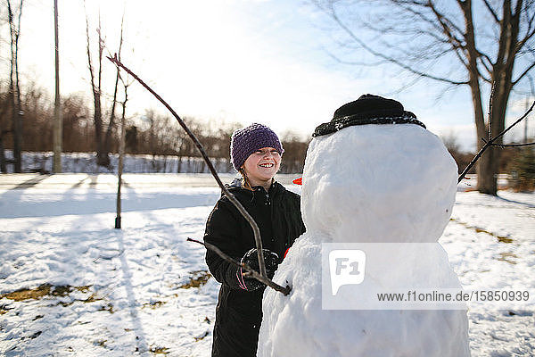 Junges Mädchen lacht den Schneemann aus  während sie ein Gesicht macht
