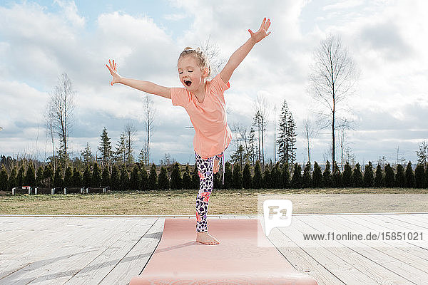 junges Mädchen balanciert auf einer Yogamatte in ihrem heimischen Hinterhof