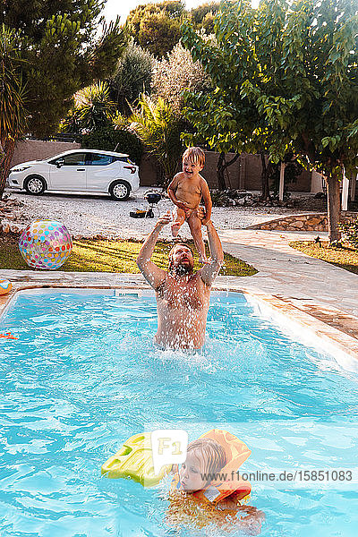 Vater schwimmt mit seinem Sohn im Pool im Hof