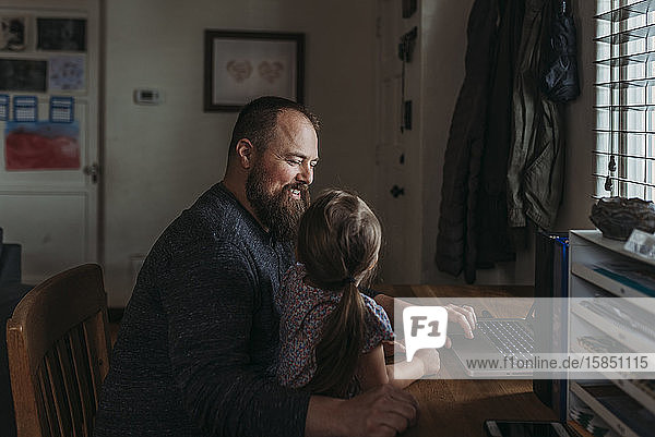 Vater mit junger Tochter im Vorschulalter sitzt  während er arbeitet