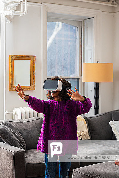 Mädchen gestikuliert beim Tragen eines Virtual-Reality-Simulators im heimischen Wohnzimmer