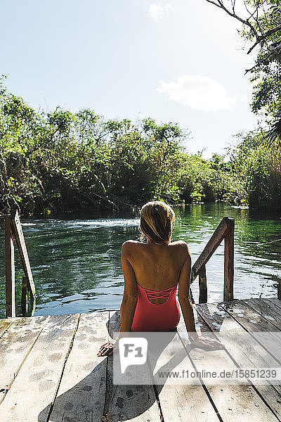 Rückenansicht einer attraktiven Frau  die in Cenote auf einem Holzpieker sitzt