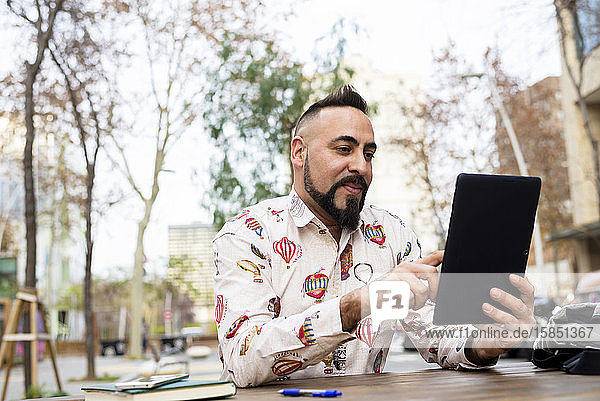 Young bearded businessman sitting at table using tablet computer