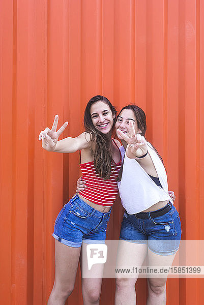 Zwei glückliche  fröhliche Teenager-Mädchen zeigen Friedensgeste