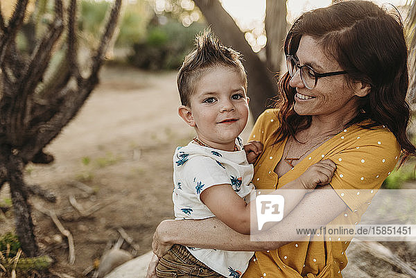 Mutter hält jungen Sohn und lächelt in hinterleuchtetem Kaktusgarten