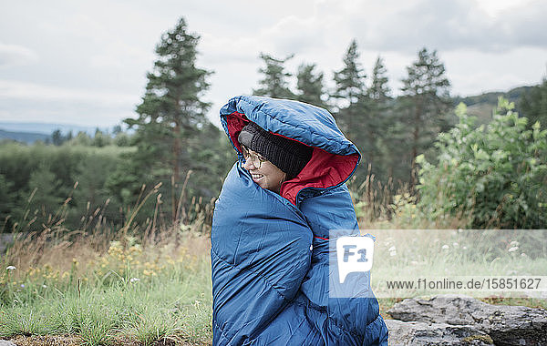 Porträt einer in einen Schlafsack gehüllten Frau beim Zelten im Freien