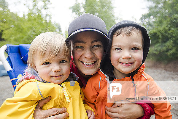 Porträt einer Mutter mit ihren beiden Kindern mit Regenjacken.