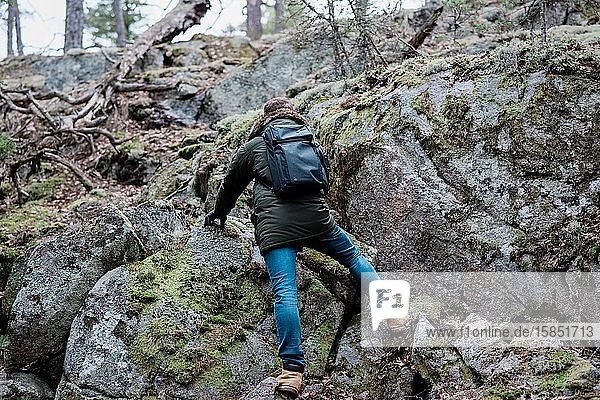 man climbing a rock whilst hiking in a forest in winter