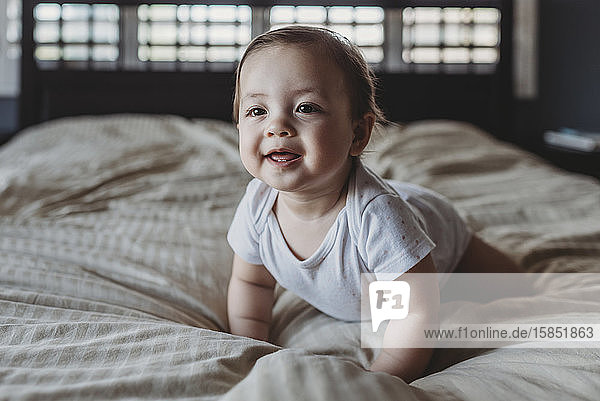 Lächelndes Baby mit zwei Zähnen  das bei Licht aus dem Fenster auf dem Bett krabbelt