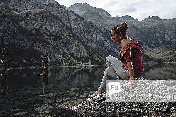Woman with bun sitting on a rock by a lake during a trip.