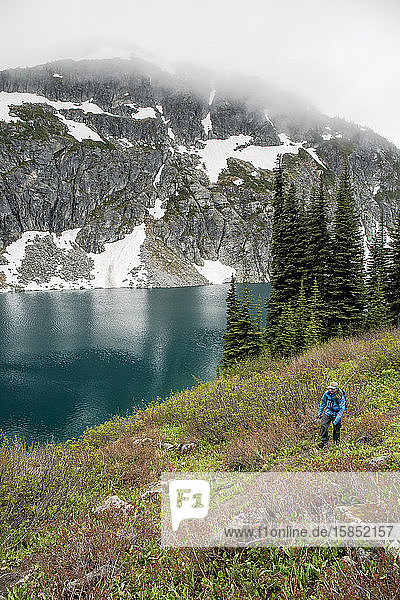 A man hikes around a beautiful alpine lake on a cloudy  rainy summer day in the Coast Mountains around Pemberton  British Columbia.