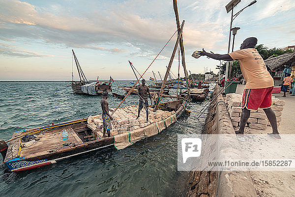 Men working throwing coral bricks from boat to the dock through air