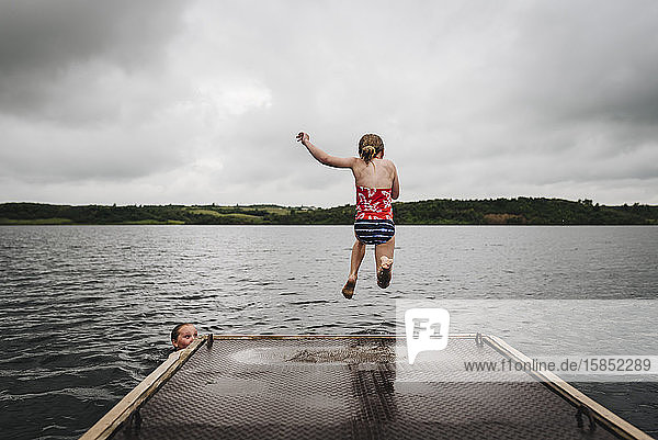 Kleine Mädchen springen an einem bewölkten Sommertag vom Dock in den See