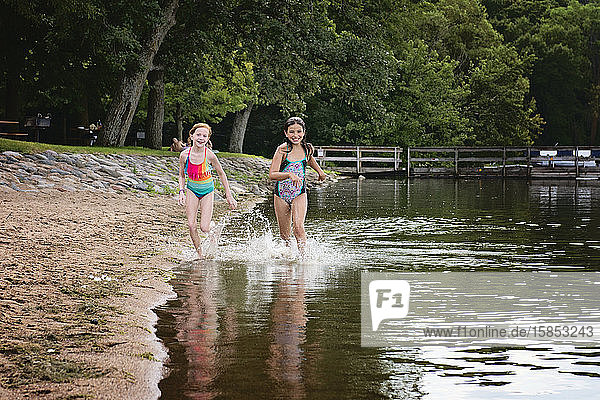 Zwei junge Mädchen in Badeanzügen laufen am Ufer eines Sees entlang