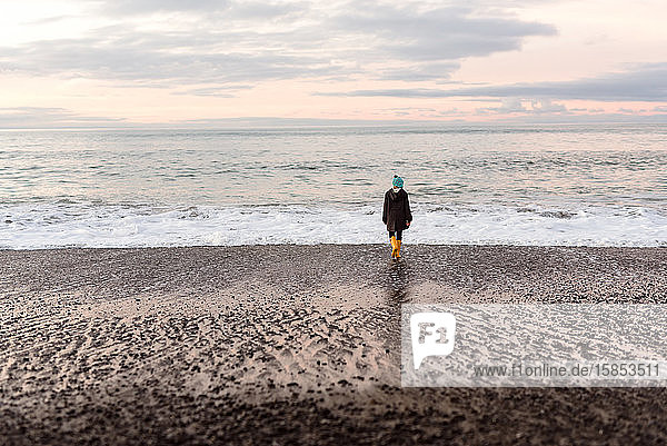 Back view of preteen girl walking on beach at dusk