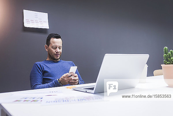 Junger Geschäftsmann liest sein Smartphone. Portrait eines Geschäftsmannes  der im Büro mit seinem Smartphone eine Nachricht liest. Mann arbeitet an seinem Schreibtisch im Büro.