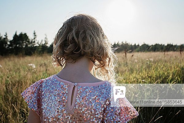 Der Rücken eines jungen Mädchens  das in einem funkelnden Kleid durch ein Feld läuft