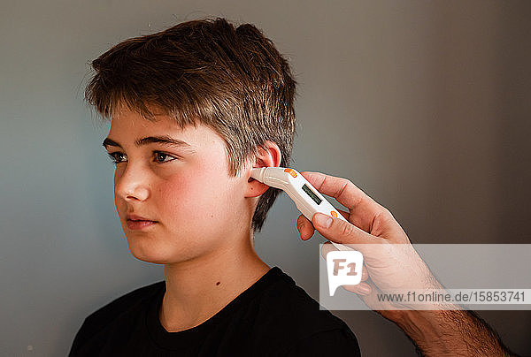 Tween boy getting temperature taken with an ear thermometer.