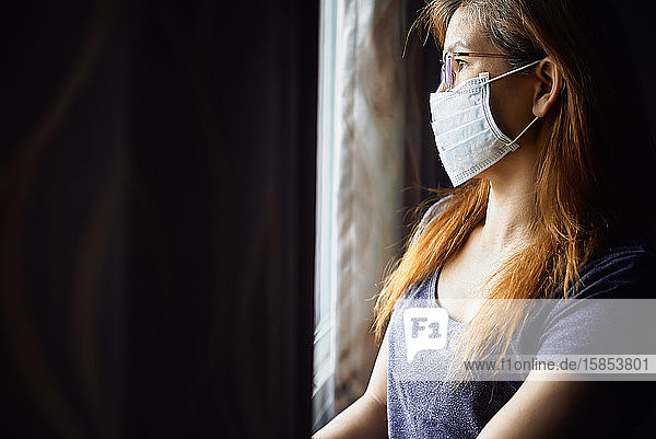 Frau mit Maske am Fenster während der COVID-19-Pandemie