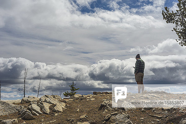 Männlicher Wanderer auf Berg stehend mit Handy und dramatischen Wolken