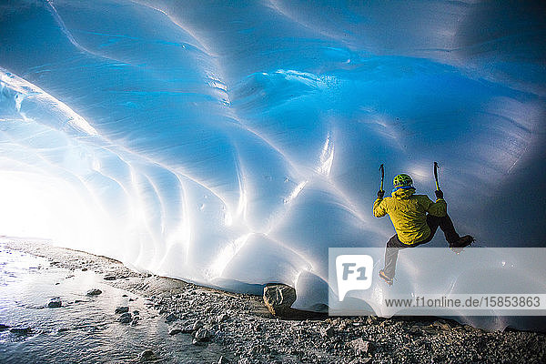 Mann klettert auf Gletschereis in Eishöhle.