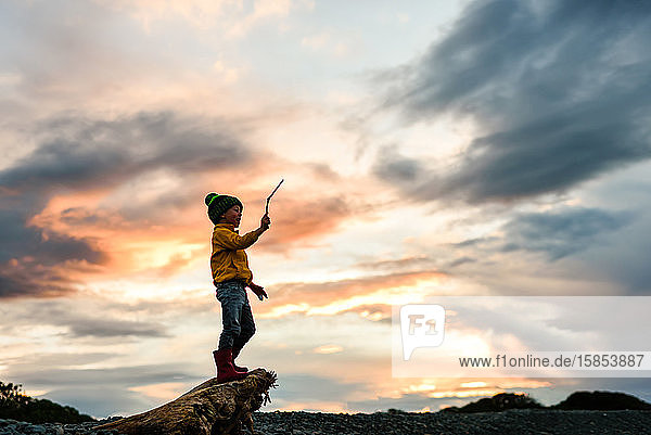 Silhouette eines kleinen Kindes  das bei Sonnenuntergang einen Stock in der Luft hält