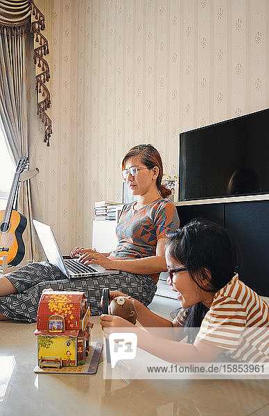 Ein Mädchen spielt in der Nähe einer Mutter  die mit einem Laptop arbeitet