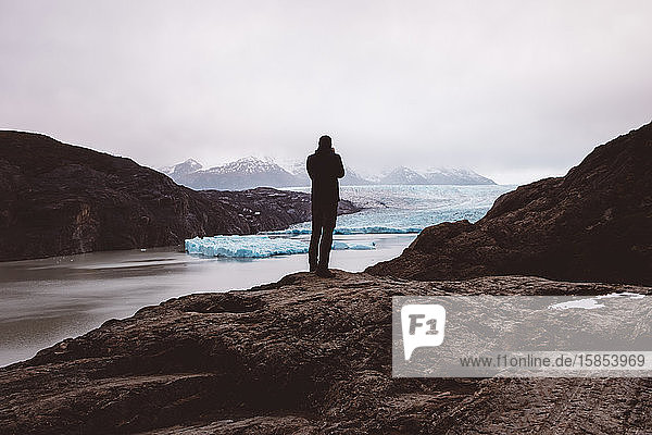 Mann steht und fotografiert auf Fels am See mit Gletschern