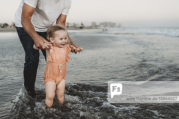 Toddler girl splashing in ocean with father at sunset