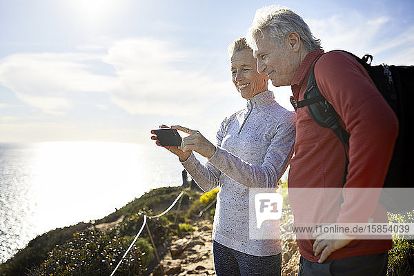 Smiling senior couple taking selfie while standing by sea against sky during sunny day