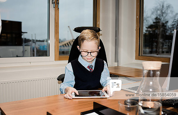 Junge schaut auf eine Tablette  während er seinem Vater in seinem Büro hilft