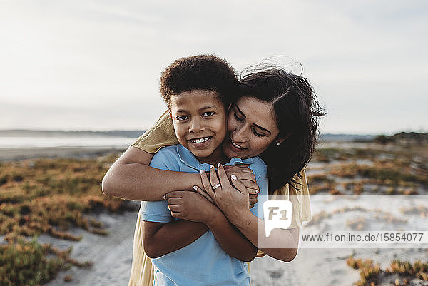 Vorderansicht Nahaufnahme-Portrait einer jungen Mutter  die ihren Sohn am Strand umarmt